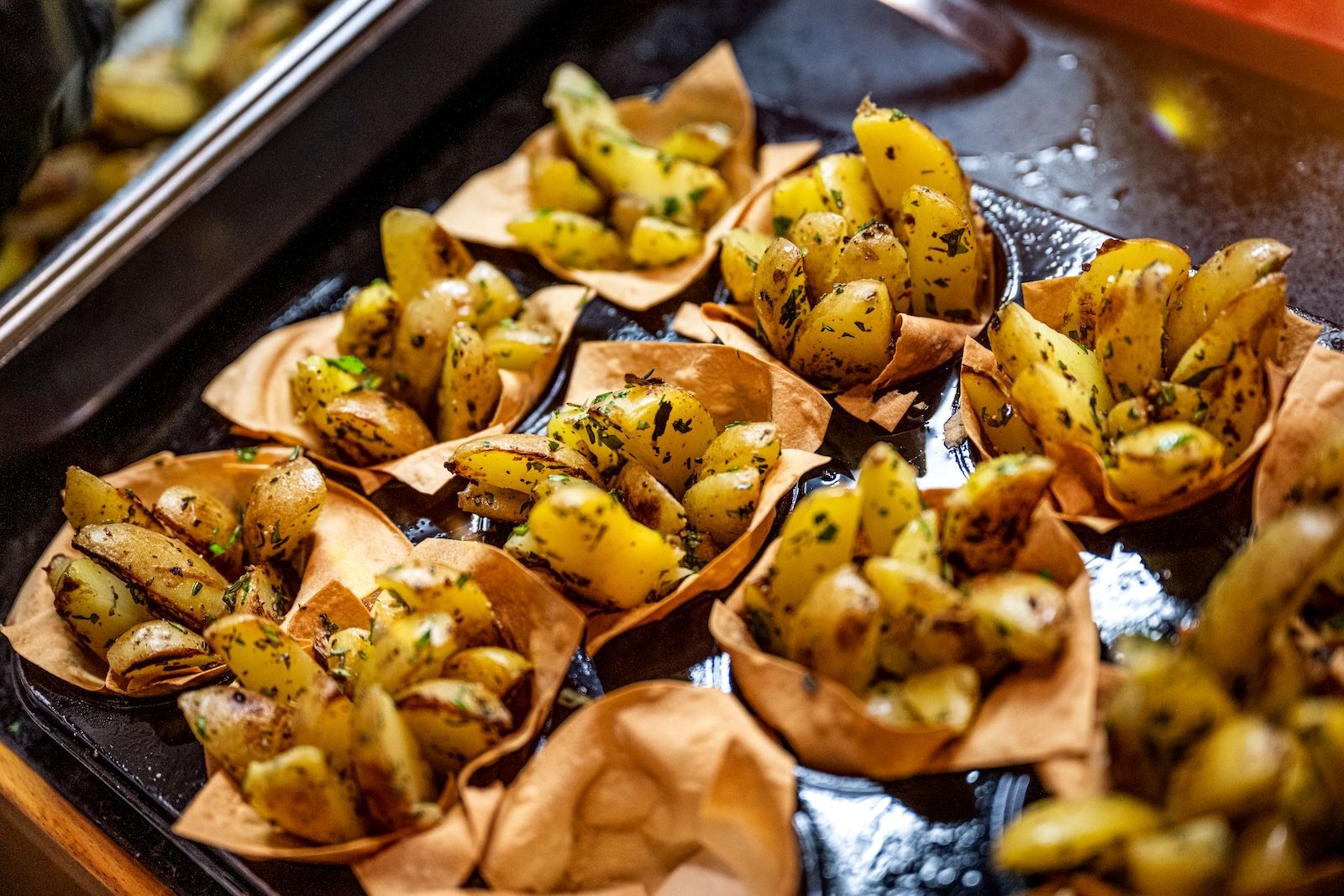 Kleine Schälchen mit goldbraun gerösteten Kartoffelspalten, angerichtet in knusprigen Teigkörbchen und mit frischen Kräutern verfeinert.